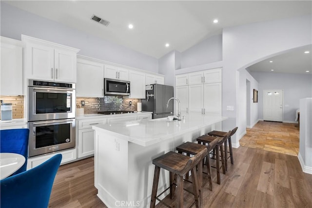 kitchen with visible vents, an island with sink, appliances with stainless steel finishes, wood finished floors, and white cabinetry