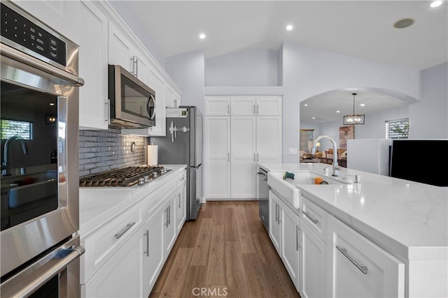 kitchen featuring arched walkways, appliances with stainless steel finishes, vaulted ceiling, white cabinetry, and a sink