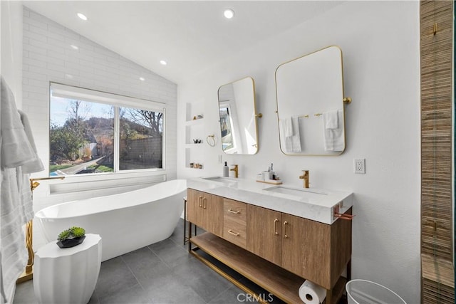 bathroom with tile patterned flooring, a sink, vaulted ceiling, a freestanding bath, and double vanity