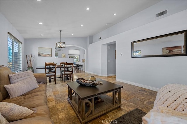 living area featuring stone tile floors, visible vents, arched walkways, baseboards, and lofted ceiling