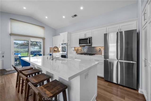 kitchen with a kitchen island with sink, dark wood-style flooring, vaulted ceiling, appliances with stainless steel finishes, and decorative backsplash