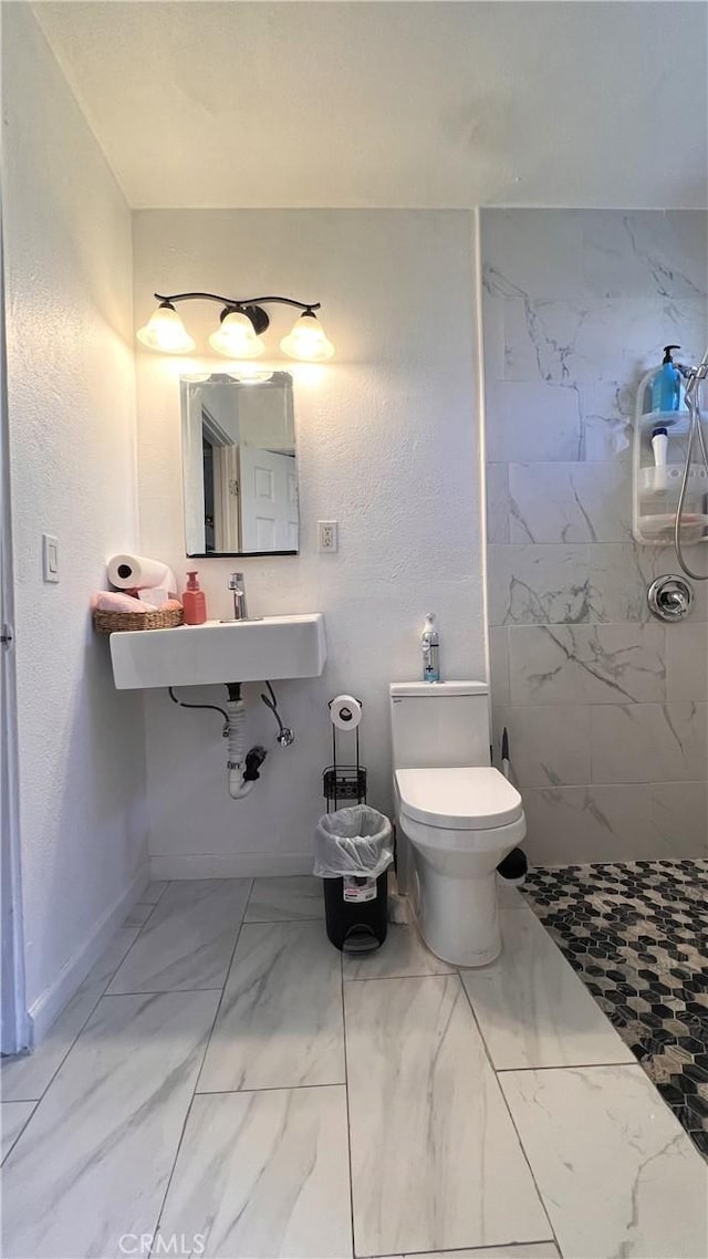 full bathroom with toilet, a sink, baseboards, marble finish floor, and tiled shower