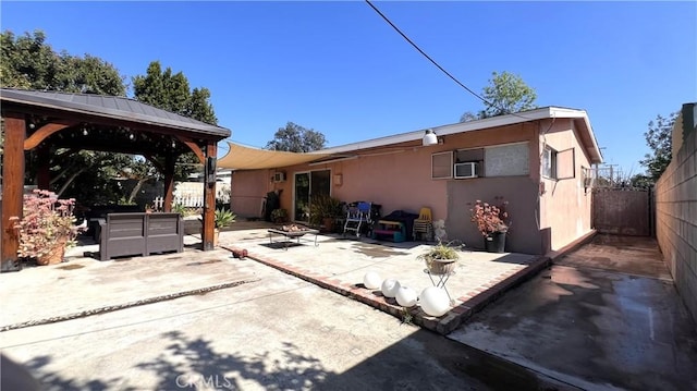 back of property featuring a fire pit, fence, a gazebo, a patio area, and stucco siding