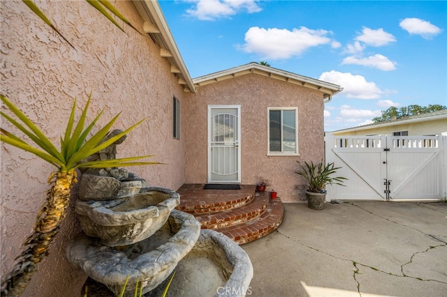 doorway to property with a gate, fence, and stucco siding