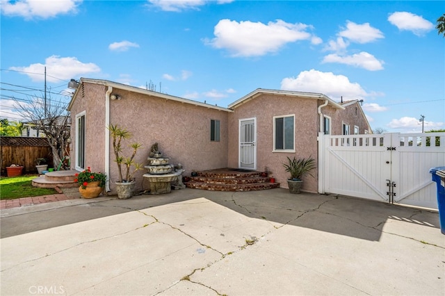 back of house featuring a gate, fence, and stucco siding