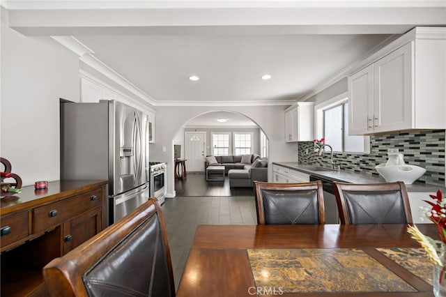 kitchen with arched walkways, decorative backsplash, stainless steel appliances, white cabinetry, and a sink