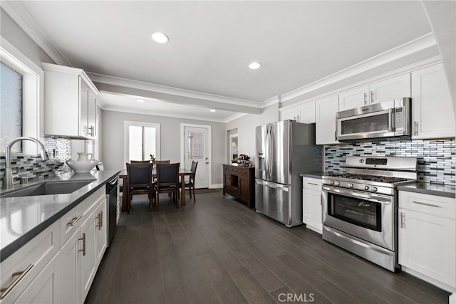 kitchen with a sink, white cabinets, appliances with stainless steel finishes, ornamental molding, and dark wood-style floors