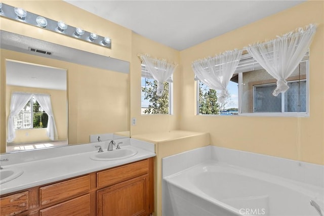 full bathroom with visible vents, double vanity, a sink, and a bath