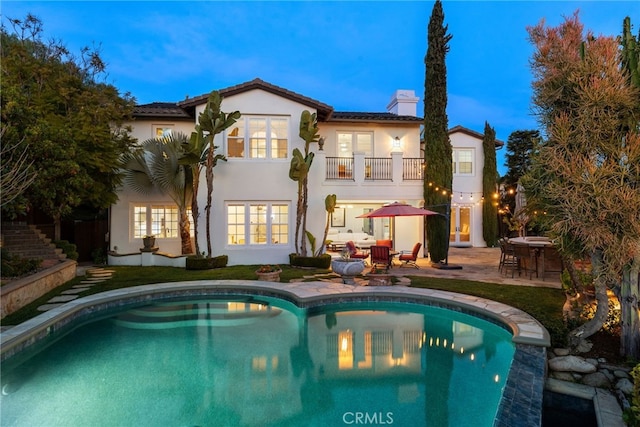 rear view of house featuring stucco siding, an outdoor pool, a balcony, a chimney, and a patio area