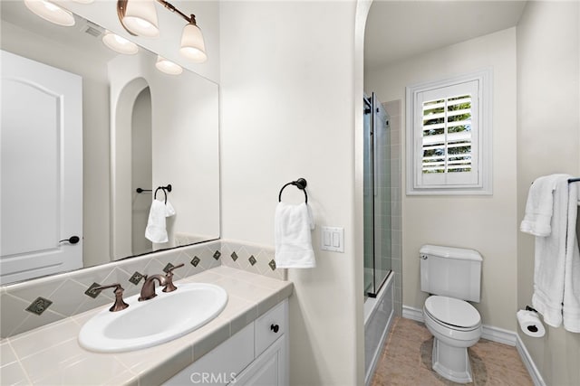 bathroom featuring vanity, baseboards, tile patterned flooring, toilet, and combined bath / shower with glass door