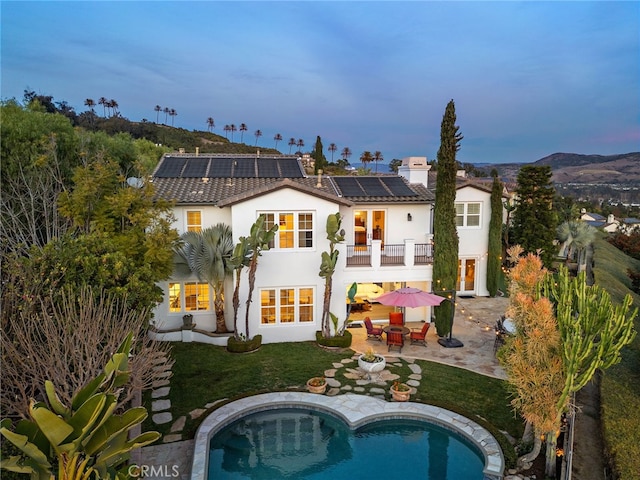 back of house at dusk with a patio, a balcony, solar panels, a yard, and stucco siding