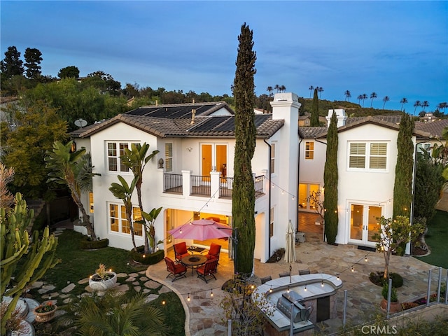 rear view of house featuring a balcony, stucco siding, french doors, a tile roof, and a patio area