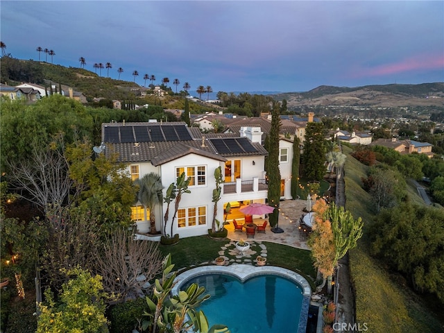 back of house at dusk with a tile roof, roof mounted solar panels, stucco siding, a patio area, and an outdoor pool