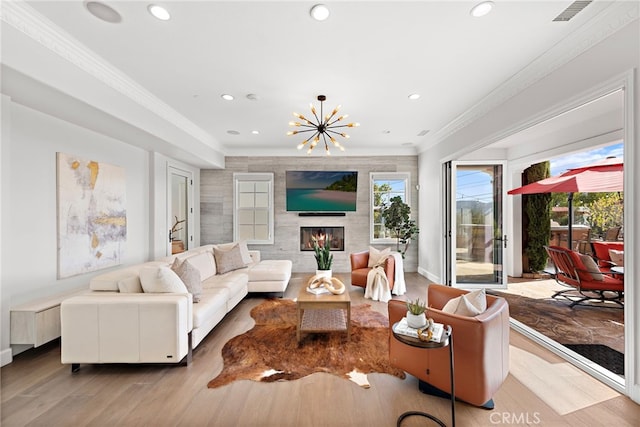 living room featuring a notable chandelier, wood finished floors, a glass covered fireplace, recessed lighting, and crown molding