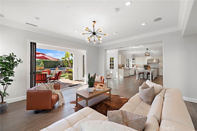 living area featuring a chandelier, visible vents, ornamental molding, and wood finished floors