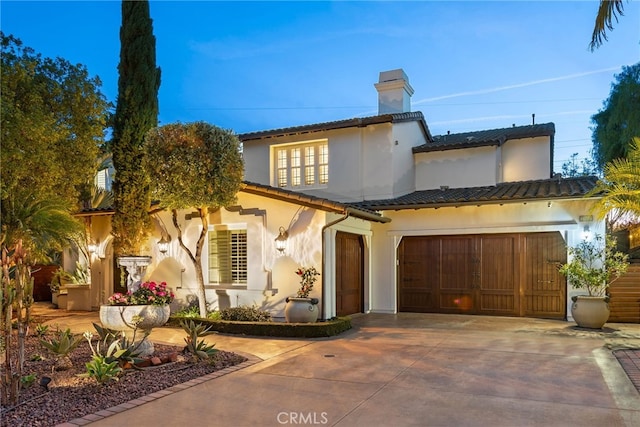 mediterranean / spanish-style house with an attached garage, a tiled roof, stucco siding, a chimney, and driveway