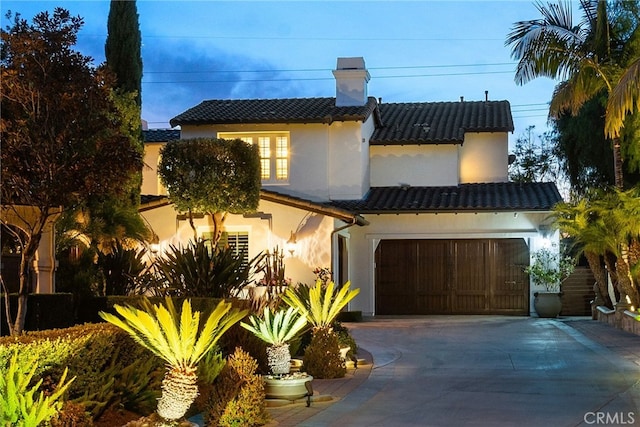 mediterranean / spanish-style home with a tile roof, concrete driveway, stucco siding, a chimney, and a garage