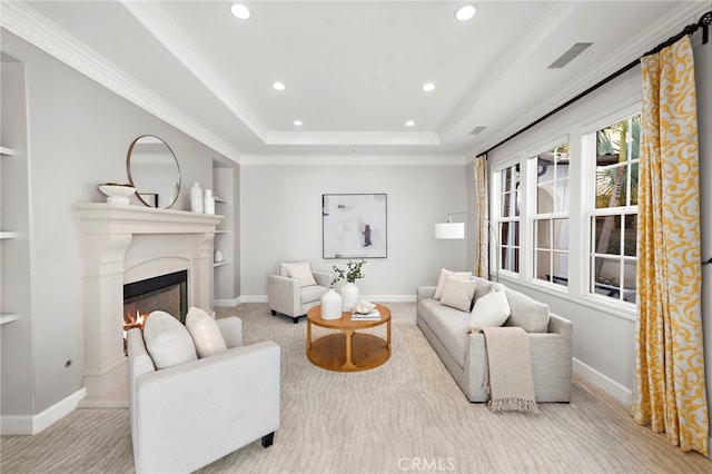 carpeted living room with visible vents, built in shelves, a tray ceiling, a warm lit fireplace, and baseboards