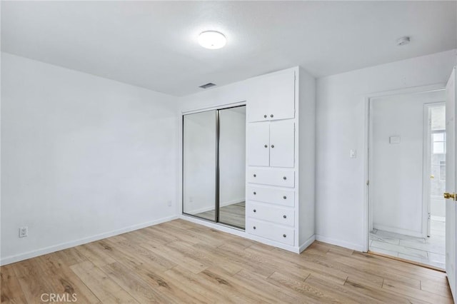 unfurnished bedroom with light wood finished floors, a closet, visible vents, and baseboards