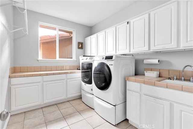 clothes washing area with cabinet space, washing machine and dryer, light tile patterned floors, and a sink