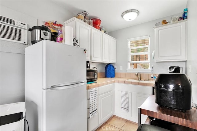 kitchen with freestanding refrigerator, white cabinets, a sink, and tile countertops