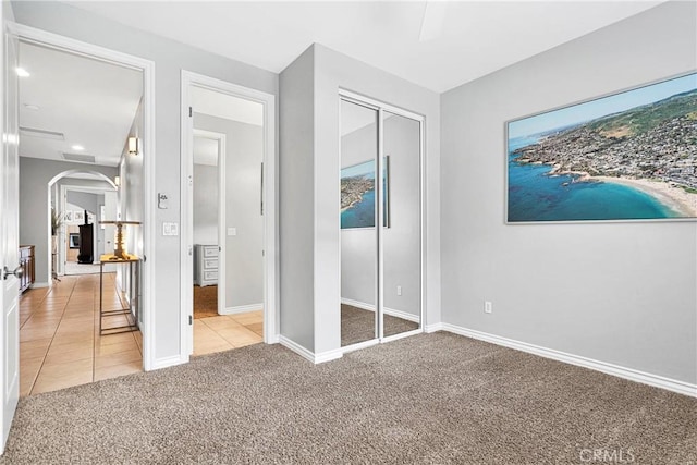 unfurnished bedroom with arched walkways, light tile patterned floors, a closet, light carpet, and baseboards