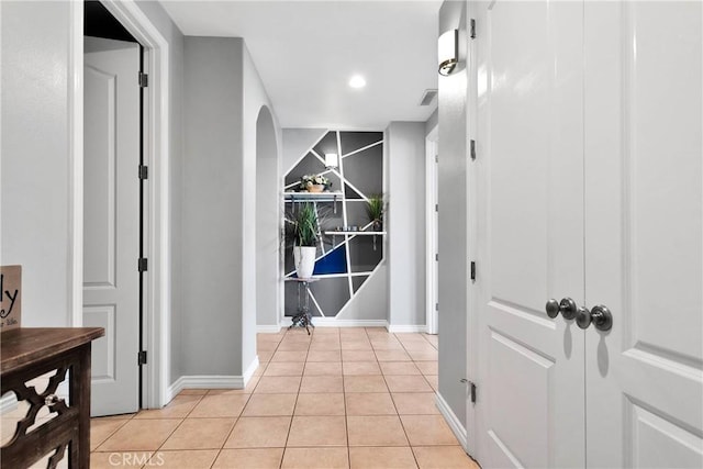 hallway featuring arched walkways, light tile patterned flooring, and baseboards