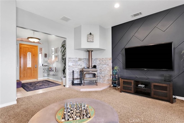 tiled living area with visible vents, carpet, a wood stove, and baseboards