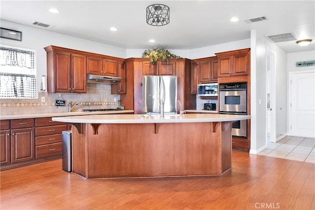 kitchen with stainless steel appliances, light countertops, visible vents, and under cabinet range hood