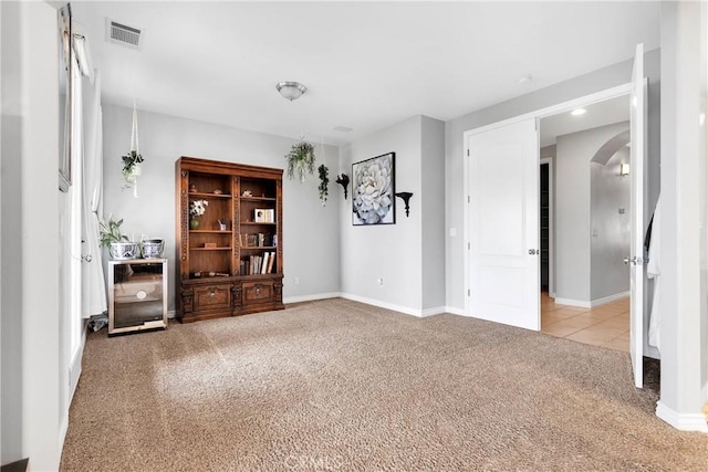 spare room featuring arched walkways, carpet flooring, visible vents, and baseboards