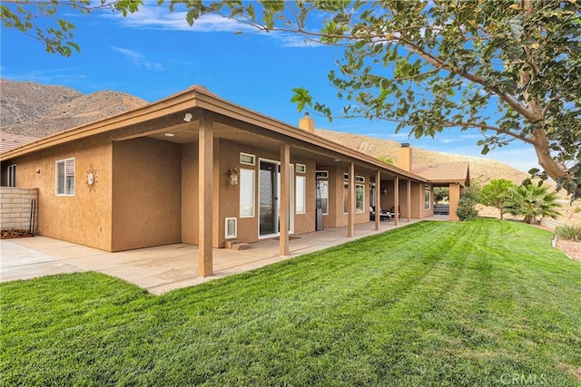 rear view of house featuring a lawn, a patio area, a mountain view, and stucco siding