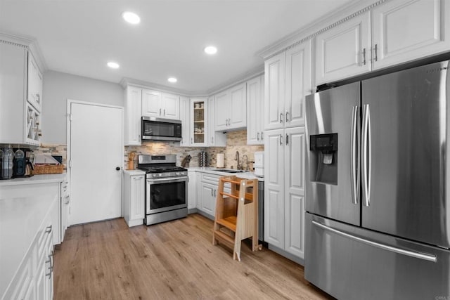 kitchen featuring stainless steel appliances, a sink, white cabinetry, light wood finished floors, and glass insert cabinets