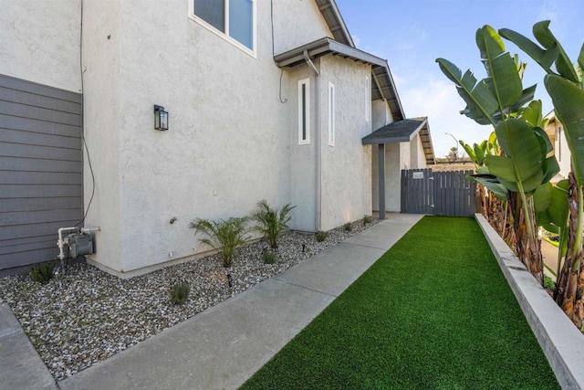 view of home's exterior with a gate, fence, a lawn, and stucco siding