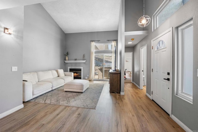 living room featuring a textured ceiling, baseboards, wood finished floors, and a glass covered fireplace