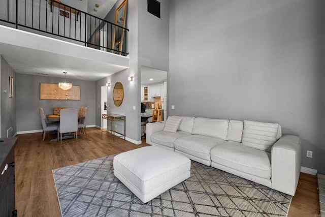 living room with a chandelier, wood finished floors, a towering ceiling, and baseboards