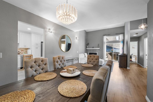 dining space featuring a fireplace, light wood-style flooring, baseboards, and an inviting chandelier