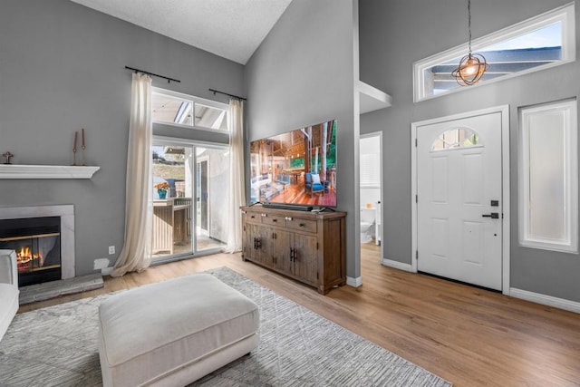 entrance foyer with baseboards, a glass covered fireplace, wood finished floors, a textured ceiling, and high vaulted ceiling