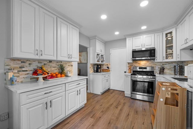 kitchen featuring stainless steel appliances, glass insert cabinets, white cabinetry, and light wood-style floors