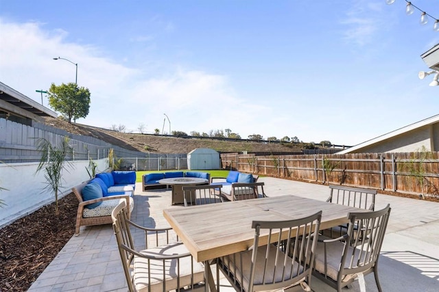 view of patio featuring outdoor dining area, a storage unit, an outdoor hangout area, a fenced backyard, and an outdoor structure