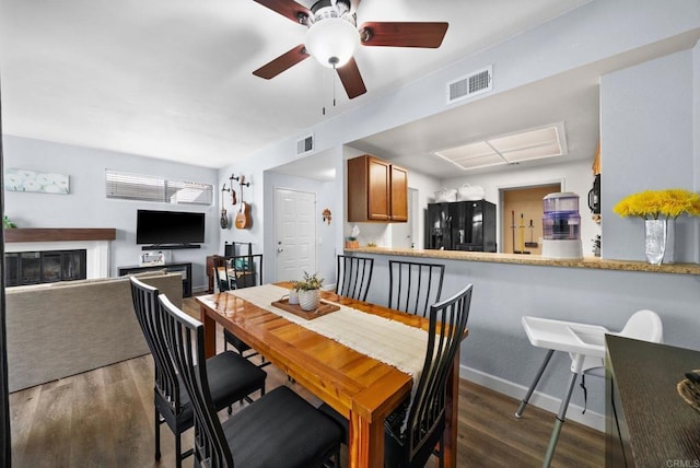 dining room featuring baseboards, visible vents, dark wood-style flooring, and a glass covered fireplace