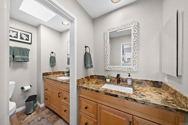 bathroom featuring toilet, a skylight, baseboards, and vanity