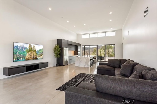 living area with recessed lighting, visible vents, concrete floors, and a high ceiling