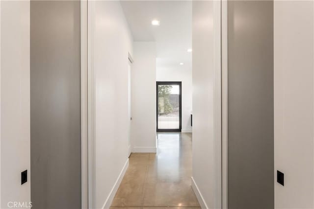 hall featuring concrete flooring, recessed lighting, and baseboards