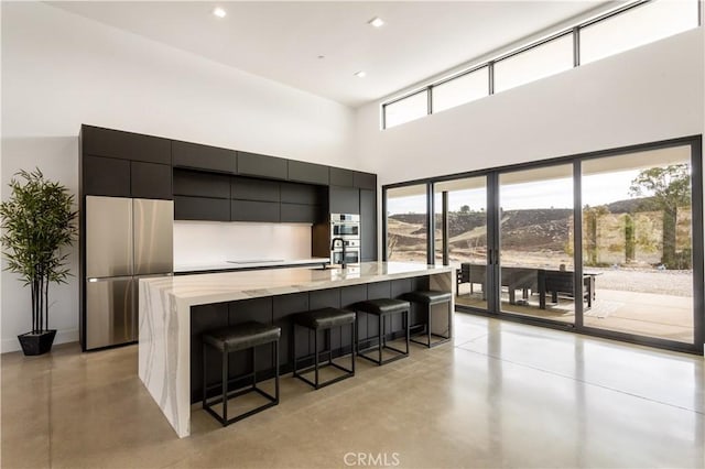 kitchen with a breakfast bar, finished concrete flooring, appliances with stainless steel finishes, modern cabinets, and a large island with sink