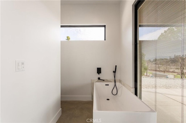 bathroom featuring concrete flooring, a bath, and baseboards