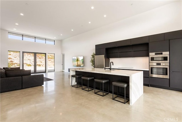 kitchen featuring a breakfast bar, a towering ceiling, light countertops, a large island, and modern cabinets