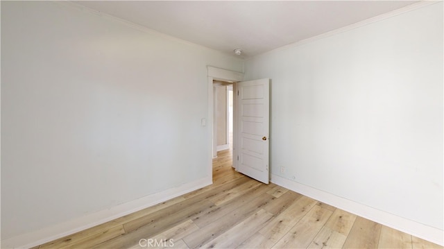 empty room with crown molding, light wood finished floors, and baseboards