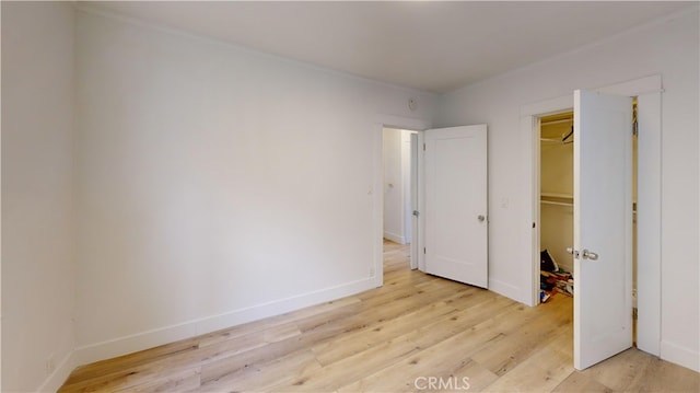 unfurnished bedroom featuring light wood-style flooring, a spacious closet, baseboards, and a closet