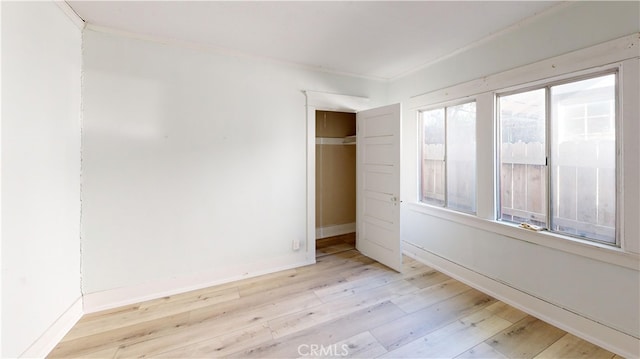 unfurnished bedroom featuring crown molding, a closet, baseboards, and wood finished floors