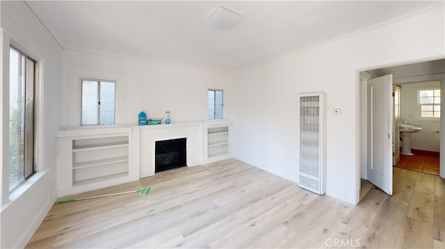 unfurnished living room with a fireplace with flush hearth, baseboards, light wood-type flooring, a heating unit, and crown molding